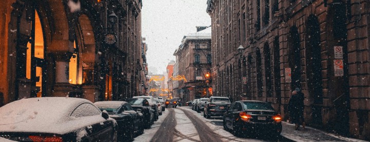 Snow gently falling on a historic street in Montreal’s Old Port, with cobblestone sidewalks, street lamps, and winter decorations – La neige tombe doucement sur une rue historique du Vieux‑Port de Montréal, avec des trottoirs pavés, des lampadaires et des décorations hivernales.