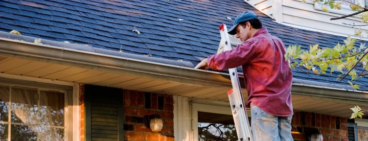 Homeowner on a ladder cleaning gutters on a Montreal house in early spring – Propriétaire sur une échelle nettoyant les gouttières d’une maison à Montréal au début du printemps.
