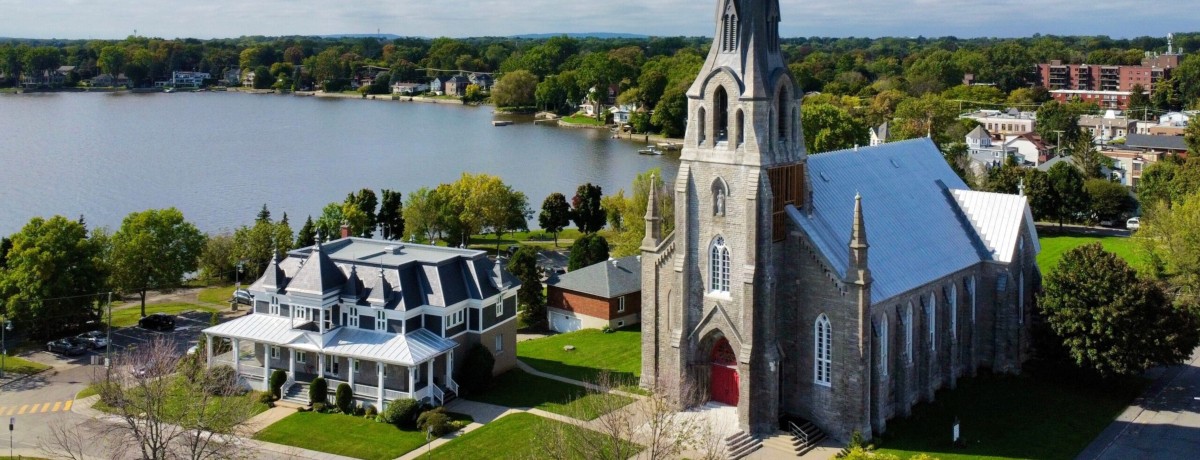 Aerial drone view of Paroisse St Joachim de Pointe Claire with the historic village and Lake Saint Louis in the background showing waterfront living in Montreal West Island | Vue aérienne par drone de la Paroisse St Joachim de Pointe Claire avec le village historique et le lac Saint Louis en arrière-plan illustrant la vie en bord de l’eau dans l’Ouest-de-l’Île de Montréal