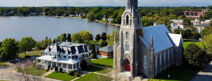 Aerial drone view of Paroisse St Joachim de Pointe Claire with the historic village and Lake Saint Louis in the background showing waterfront living in Montreal West Island | Vue aérienne par drone de la Paroisse St Joachim de Pointe Claire avec le village historique et le lac Saint Louis en arrière-plan illustrant la vie en bord de l’eau dans l’Ouest-de-l’Île de Montréal