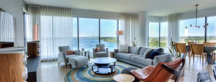 Luxury condo living room at Symphonia POP in Île-des-Sœurs with panoramic views of the St. Lawrence River, South Shore and Downtown Montreal. Salon d'un condo de luxe au Symphonia POP à Île-des-Sœurs offrant une vue panoramique sur le fleuve Saint-Laurent, la Rive-Sud et le centre-ville de Montréal.